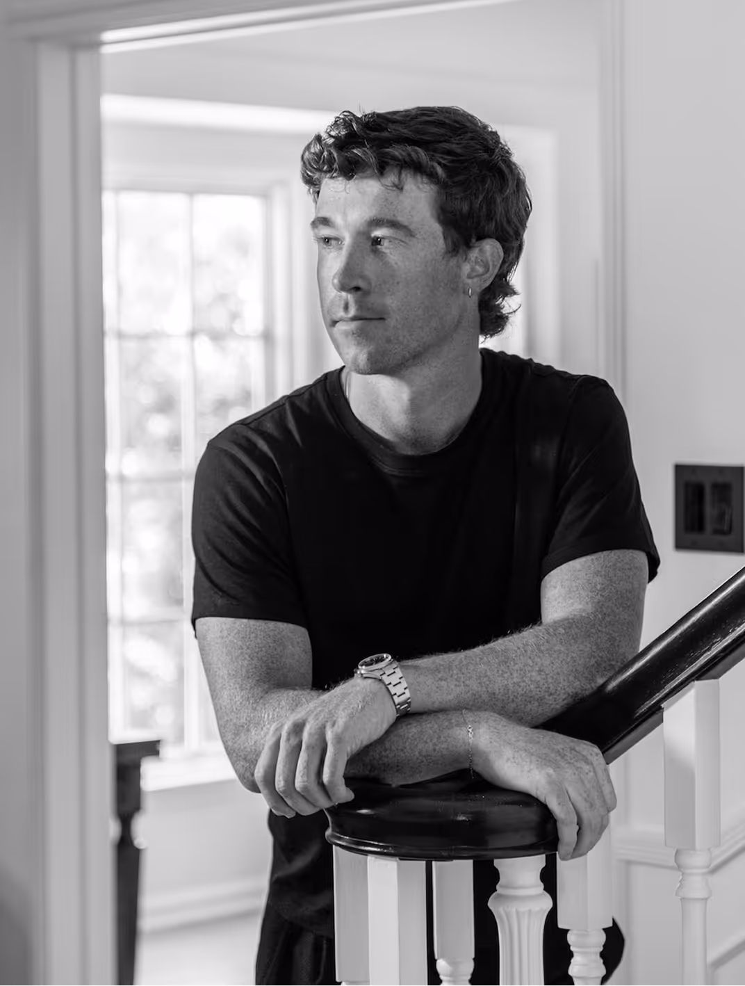 Duke Butler, founder of Duke Talent, in a black tee resting on a stair rail in a sunlit hallway.